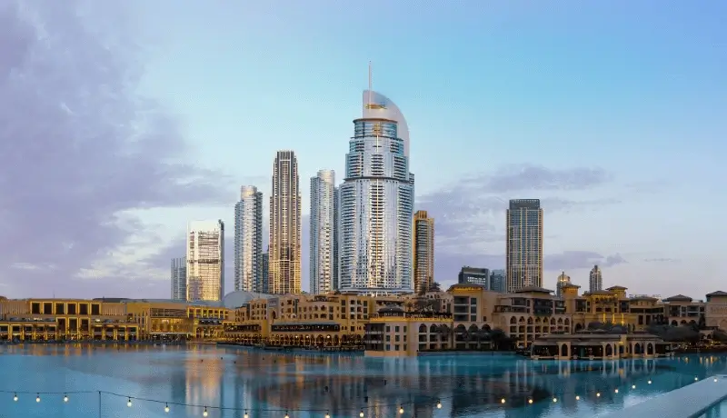 Waterfront view of a cluster of sleek high‑rise towers under a soft blue sky